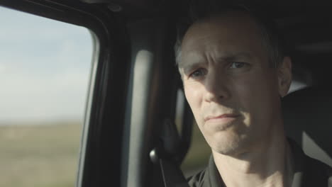 closeup of a man riding in a car with a concerned expression as he looks ahead and then out the window