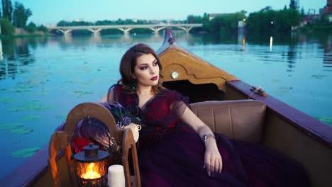 elegant female with perfect make-up and beautiful dress riding a boat on the background of a bridge over the river. pretty young lady floating in gondola in the evening