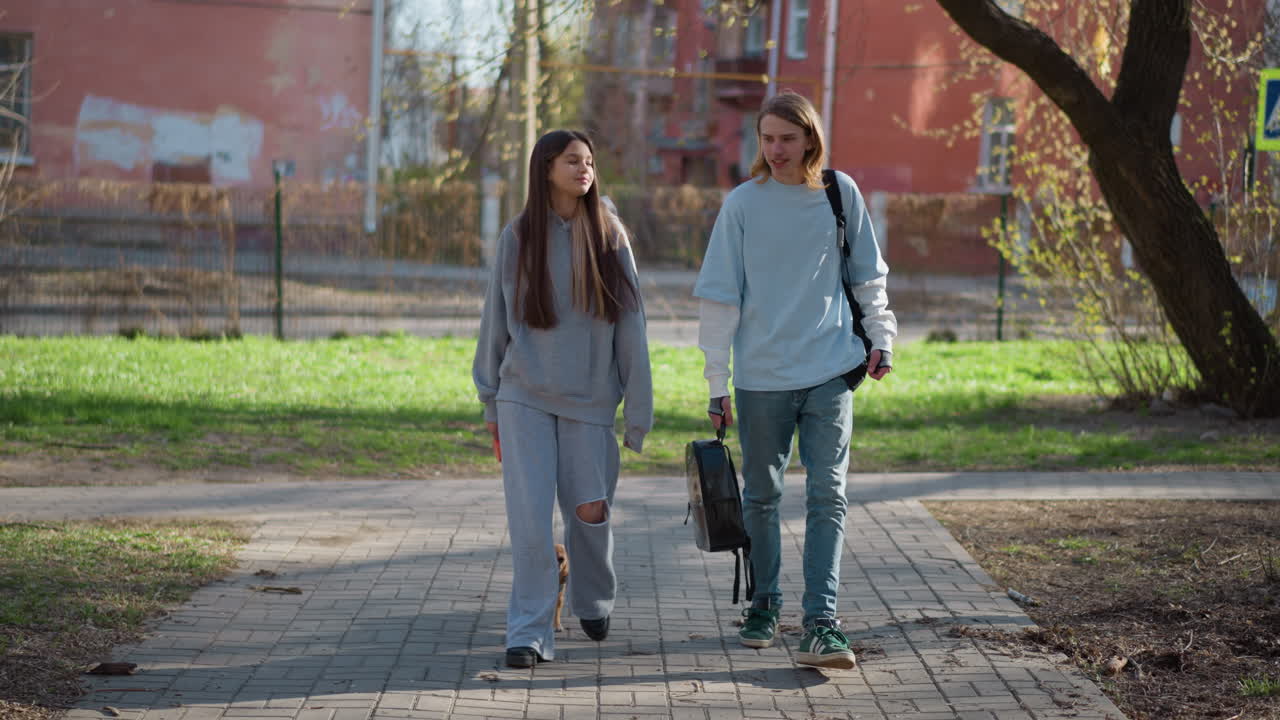 pareja paseando a un perro pequeño cerca de la ciudad; amigos informales paseando a su pequeña mascota cerca de la arquitectura de la ciudad; hombre y mujer paseando tranquilamente cerca de edificios con su diminuto perro cerca del parque