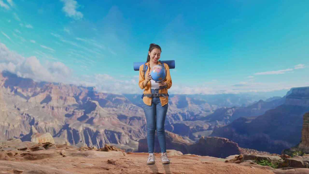 Full Body Of Asian Female Hiker With Mountaineering Backpack Holding World Globe In Her Hands And Smiling While Traveling At The Top Of Mountain