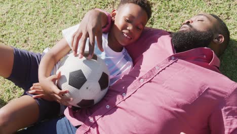 happy african american father and son playing soccer in garden, in slow motion