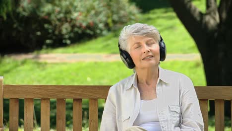 Old-female-listening-to-music-with-headset-on-a-bench