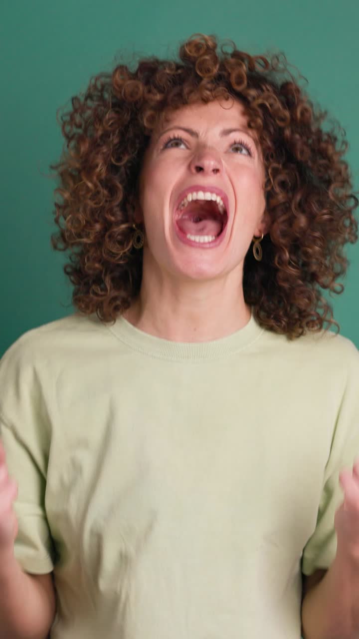 Shocked young woman showing stretched hands with palms on green background. Vertical orientation