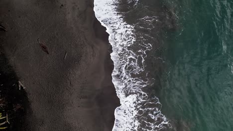 caribbean water washing volcanic dark beach of guadeloupe, aerial top down