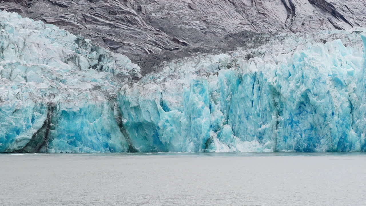 This is a close-up shot of a piece of the blue ice wall calving off the Dawes Glacier in Endicott Arm near Juneau Alaska. It shows white seagulls flying around showing scale