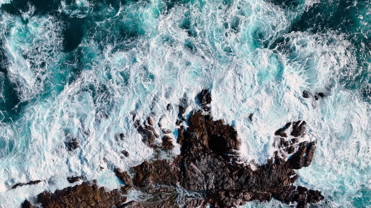 Veduta aerea ravvicinata di onde oceaniche e schiuma. Vista dettagliata dall'alto di acqua di mare turchese e schiuma bianca che si infrange contro le rocce a Big Sur, California