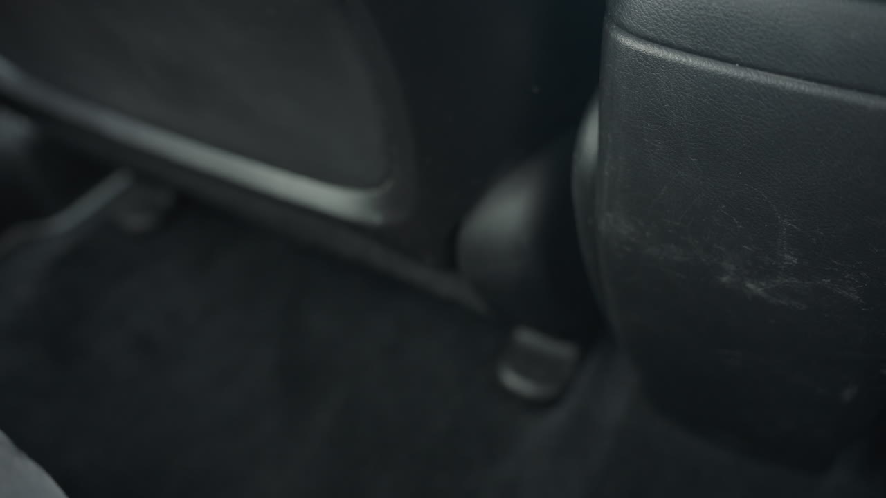 close up of driver seat sliding back and forth on black carpeted car floor with natural daylight entering vehicle interior and creating soft highlights on textured surfaces