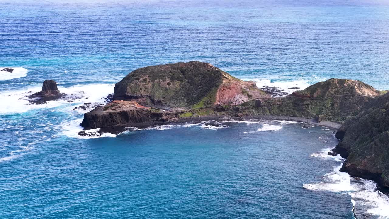 Drone camera glides above rugged coastal cliffs, turquoise ocean, and dramatic rock formations in daylight