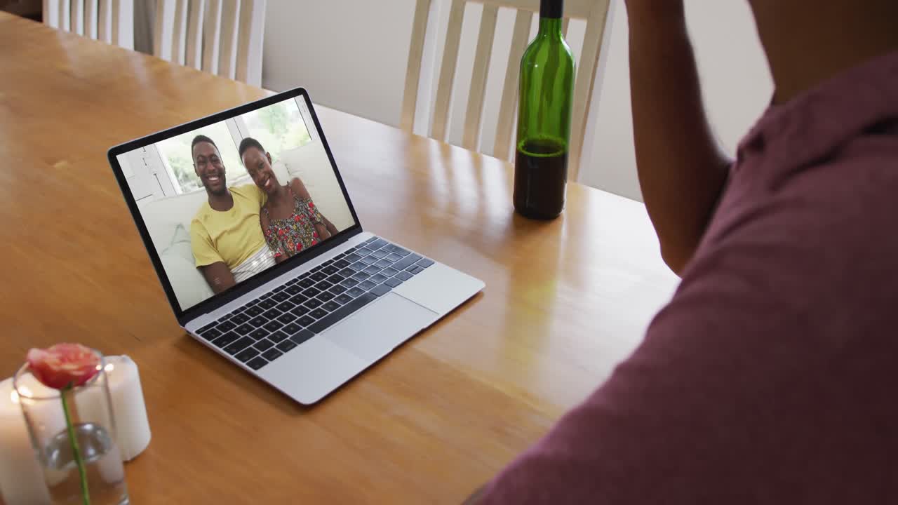 Mixed race man sitting at table using laptop making video call with friends
