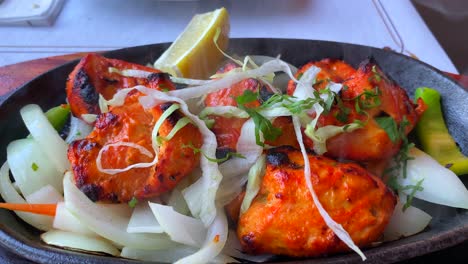 Pollo-Tandoori-Indio-Tradicional-Con-Cebollas-En-Un-Plato-Muy-Caliente-Con-Humo-De-Vapor-En-Un-Restaurante,-Tiro-Estático-De-4k