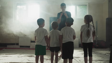 trainer shows boxing stances to children in gym. interested little students listen to sensei instruction before exercising in smoky club slow motion