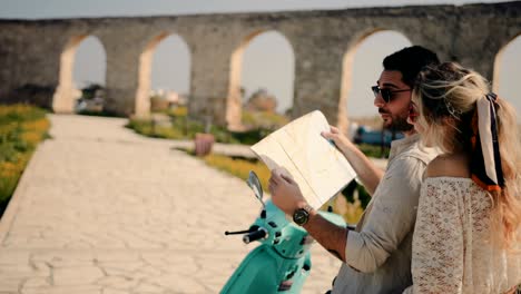 young tourists couple on retro scooter reading map for directions