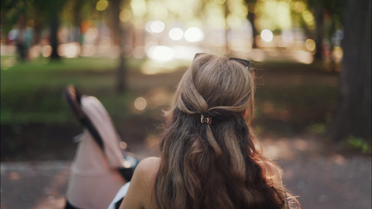 A mother with long wavy hair siting on a bench, breastfeeding her baby in a peaceful park, next to a modern baby stroller