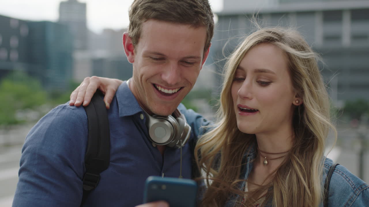 portrait of happy young caucasian couple in city posing making faces taking photo using smartphone enjoying urban travel lifestyle