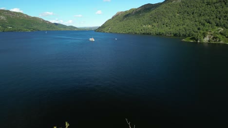 volando bajo sobre una pequeña isla en un lago oscuro rodeado de montañas boscosas luego sobre un pequeño ferry en un brillante día de verano