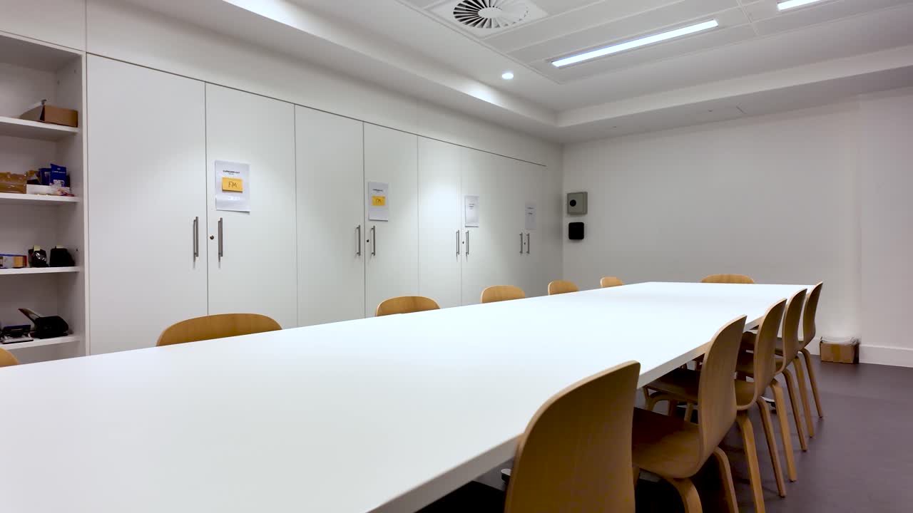 Bright Office Interior With Long White Meeting Table And Wooden Chairs Featuring White Cupboards And Shelves For Corporate Or Educational Purposes