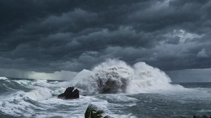 Plan large dramatique de vagues déferlantes contre des rochers sous un ciel orageux, capturant la puissance brute.