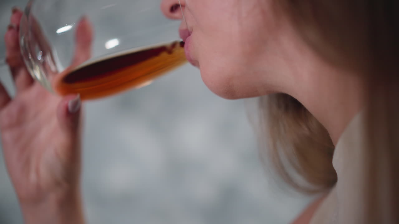 Upward view of woman chewing food while gently sipping red wine from glass showing slow relaxed movement in casual setting with natural soft background