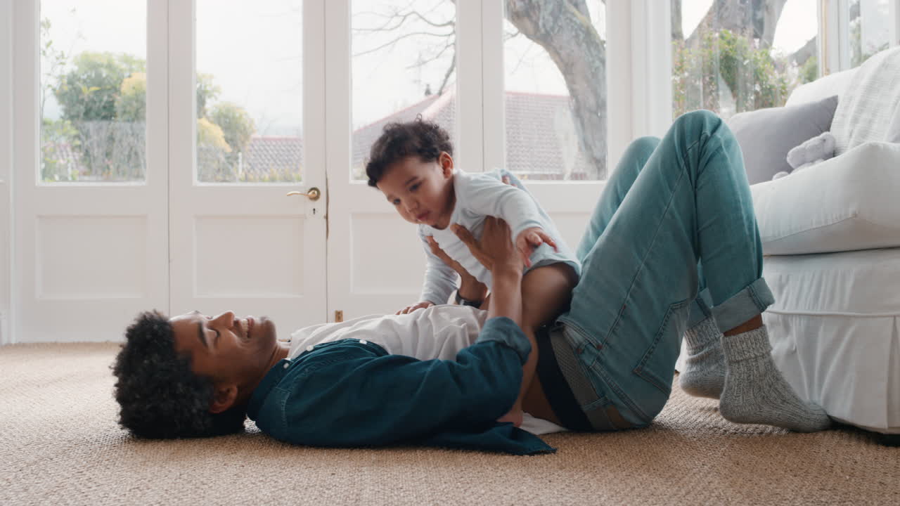 glücklicher vater, der zu hause mit seinem baby spielt, sich amüsiert, das kleinkind in den händen hält, lächelnder vater, der die vaterschaft genießt 4k