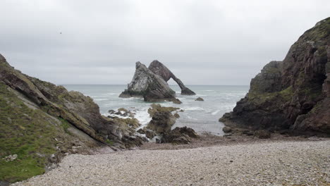 Drohnenantenne,-Die-Rückwärts-Von-Einem-Riesigen-Felsen-Im-Meer-Zum-Felsigen-Strand-Fliegt