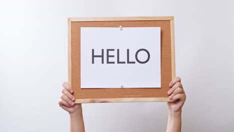 woman's hand shows the paper on board with the word hello in white studio background with copy space