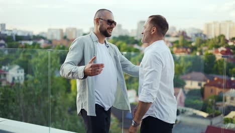 Two-happy-businessmen-meet-on-the-terrace-overlooking-the-city-and-shake-hands