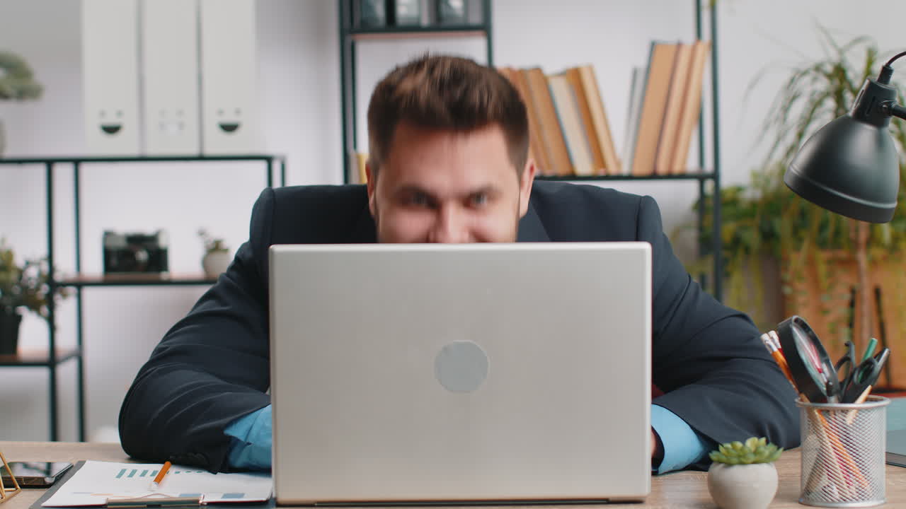 Office businessman hiding behind laptop computer making funny silly face fooling around disrespect