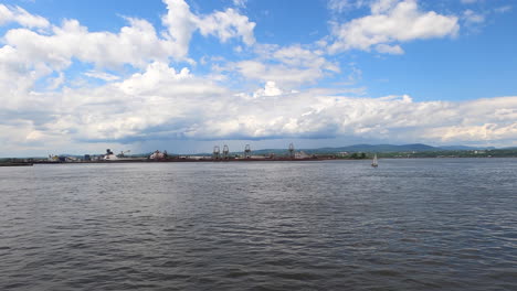 wide view of sailboat in distance sailing along coast port with cloudy sky in horizon, quebec region