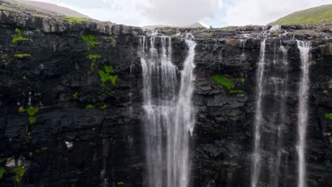 a stunning cascading waterfall surrounded by rugged cliffs and moss, faroe islands