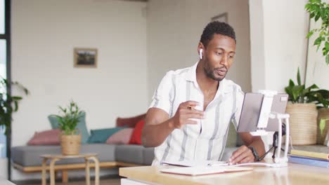 Happy-african-american-man-sitting-at-table-in-kitchen,-using-tablet-and-making-vlog