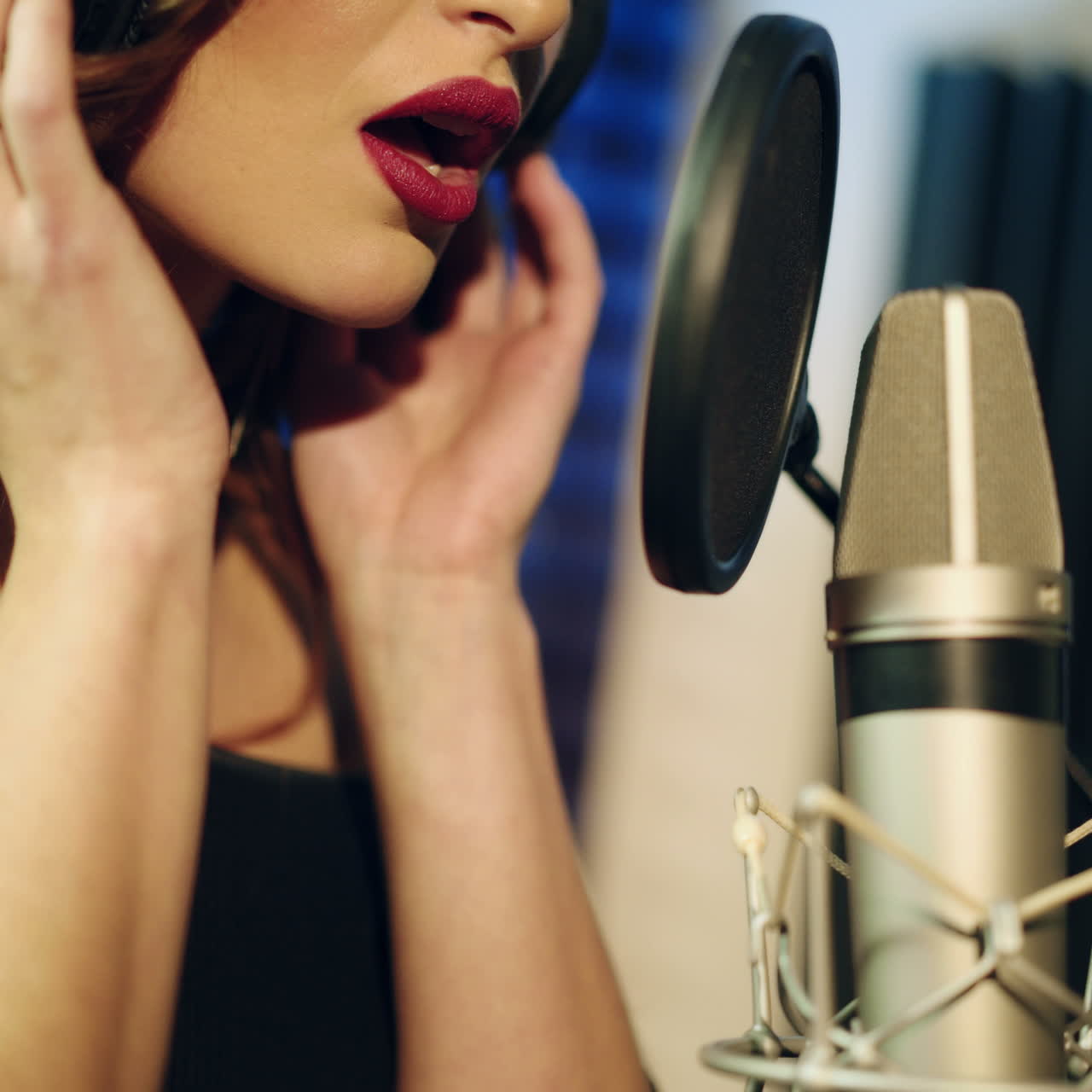 Beautiful woman with headphones singing close to the mic in the studio. Professional white and black microphone and female's face with bright lips. Close-up.