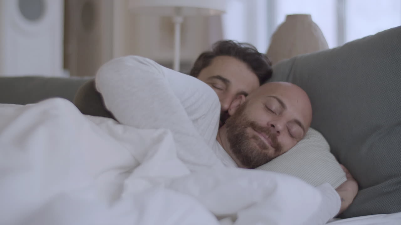 pareja homosexual acostada bajo una manta por la mañana y abrazándose