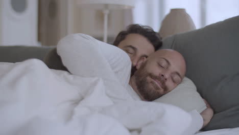Homosexual-couple-lying-under-blanket-in-morning-and-hugging