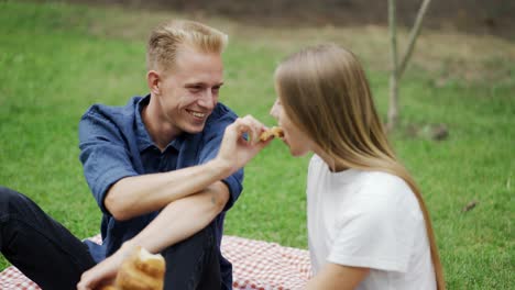 A-guy-teases-a-girl-while-feeding-her-at-a-picnic.-Go-to-the-park.-Romantic-date.-cheerful-couple