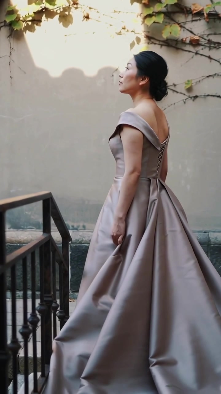 Video verticale: Donna con abito di pizzo che scende le scale di un cortile, sollevando la gonna verso il sole