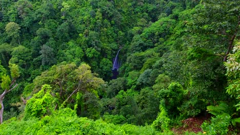 Vista-Aérea-Del-Hombre-Parado-En-Un-Mirador,-Volando-Un-Dron-Hacia-La-Cascada-Tiu-Kelep,-En-Lombok