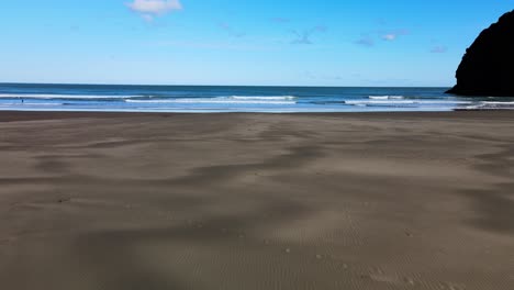 Volando-A-Través-De-Las-Texturas-De-La-Playa-De-Arena-Negra-De-Piha-Y-Hacia-El-Famoso-Surf-Break