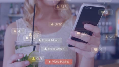 Animación-De-íconos-De-Medios-Sobre-Una-Mujer-Caucásica-Con-Bebida-Usando-Un-Teléfono-Inteligente