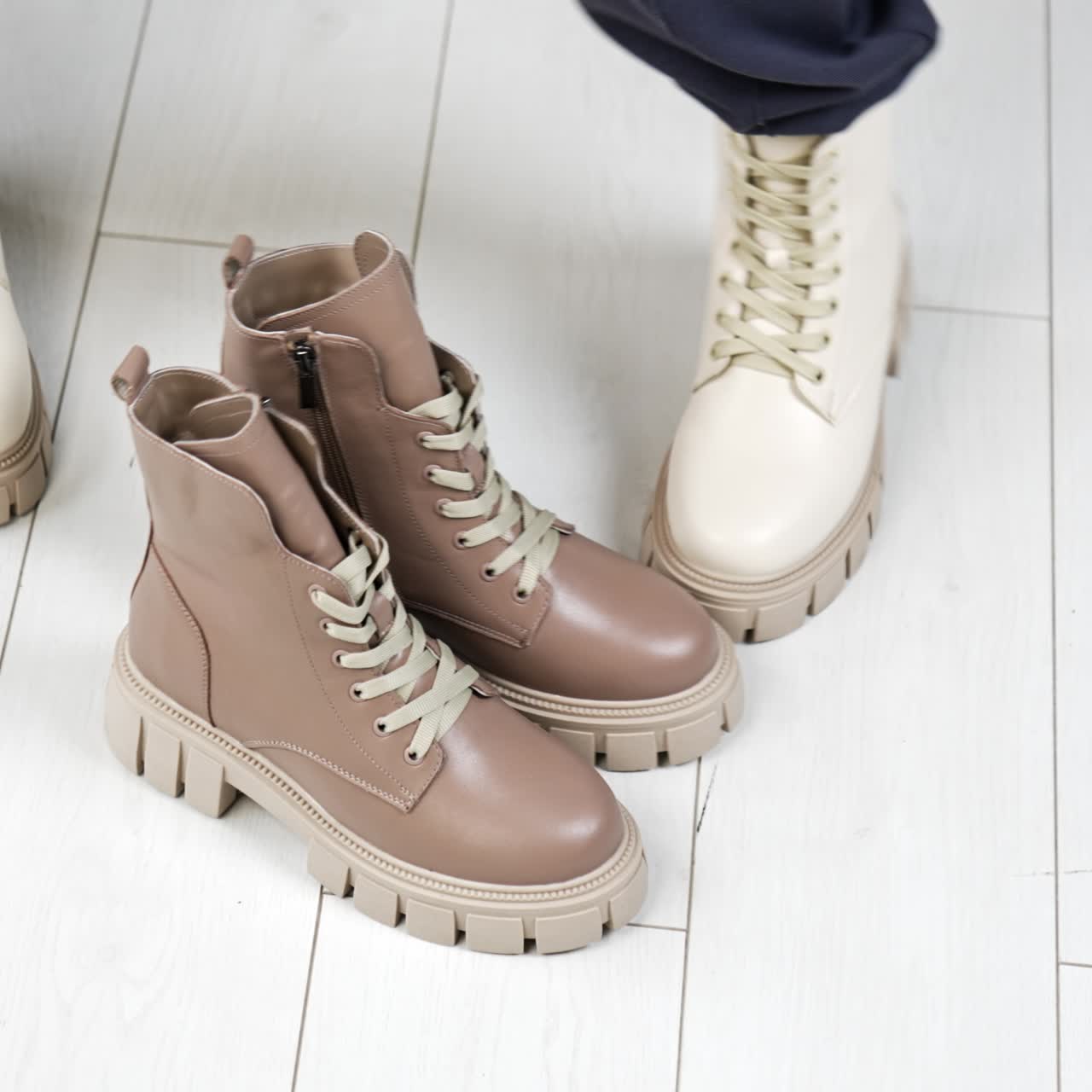 Model puts on the floor a similar beige pair of boots to those she's wearing. Female demonstrating stylish modern footwear. Top view