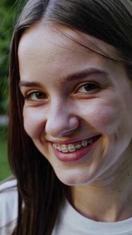 confident teenage girl with metal braces radiating happiness while standing in lush green park, showcasing genuine joy and positive self image during adolescent years