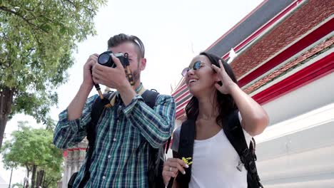 young couple tourist backpackers taking pictures at thai temple in thailand