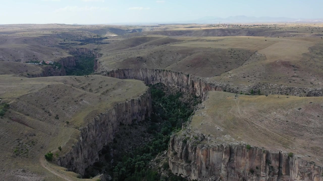 Ripresa aerea con drone ad alta quota del drammatico canyon della Valle di Ihlara con ripide scogliere rocciose che circondano un bacino forestale verde lussureggiante che attraversa pianure aride dell'altopiano ad Aksaray, Turchia.
