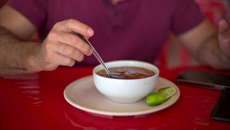 Zeitlupe-Nahaufnahme-Eines-Lateinamerikanischen-Mannes,-Der-Seine-Barbacoa-Brühe-Mit-Einem-Löffel-In-Einem-Restaurant-In-Mexiko-Rührt