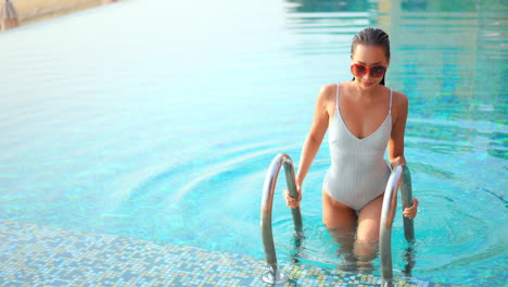 Hermosa-Mujer-Asiática-En-Traje-De-Baño-Blanco-Sale-De-La-Piscina-Acariciando-El-Cabello-Mojado