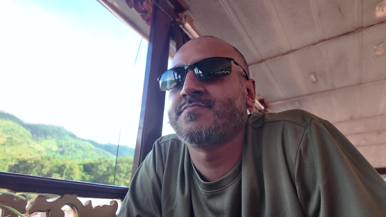 Muž s vousy z jižní Asie plující na pomalé lodi v Laosu a užívající si zážitek z cestování po řece Mekong