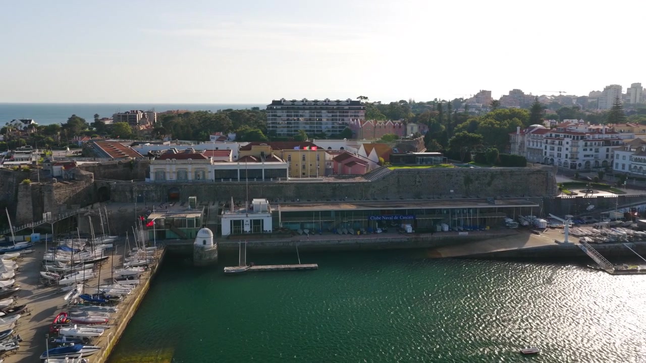 Vista de dron con vistas a la Marina de Cascais, el paseo marítimo de la Ciudadela y veleros anclados en Cascais, Portugal, durante la cálida luz de la hora dorada en la costa atlántica.