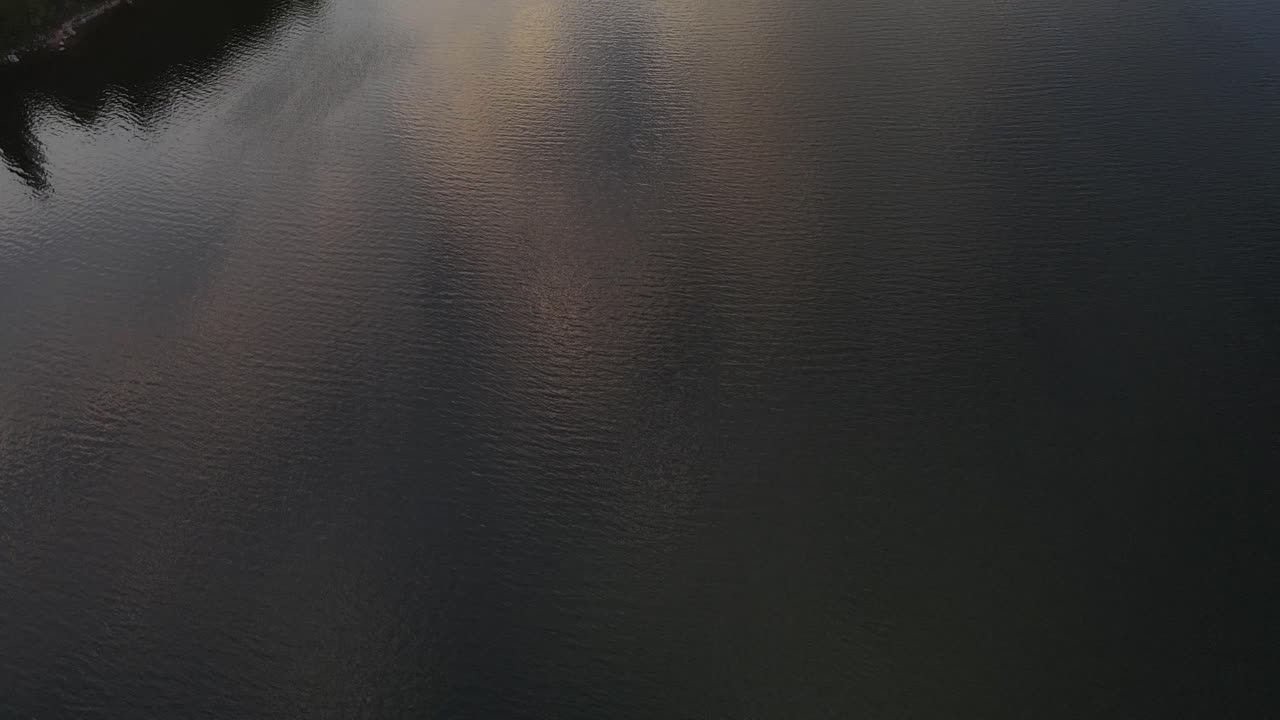 drone filming schluchsee lake and tilting up to reveal the sunset and a small sailing yacht, schwarzwald Deutschland