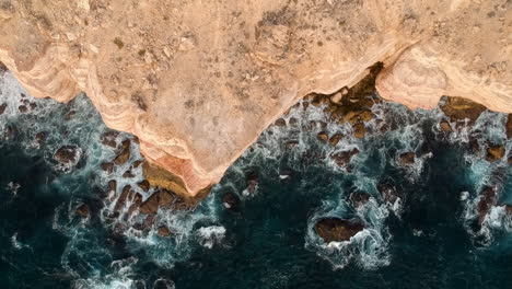 cinematic drone video from cliff in outback desert during sunset golden hour with big blue waves and green trees