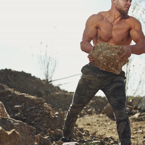 healthy bodybuilder doing workout with stones. strained muscular athlete throwing big stones on the rocky background. slow motion.