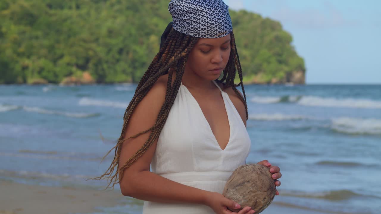 바다의 파도를 배경으로 손에 들고 있는 코코넛을 바라보는 예쁜 젊은 여성의 확대